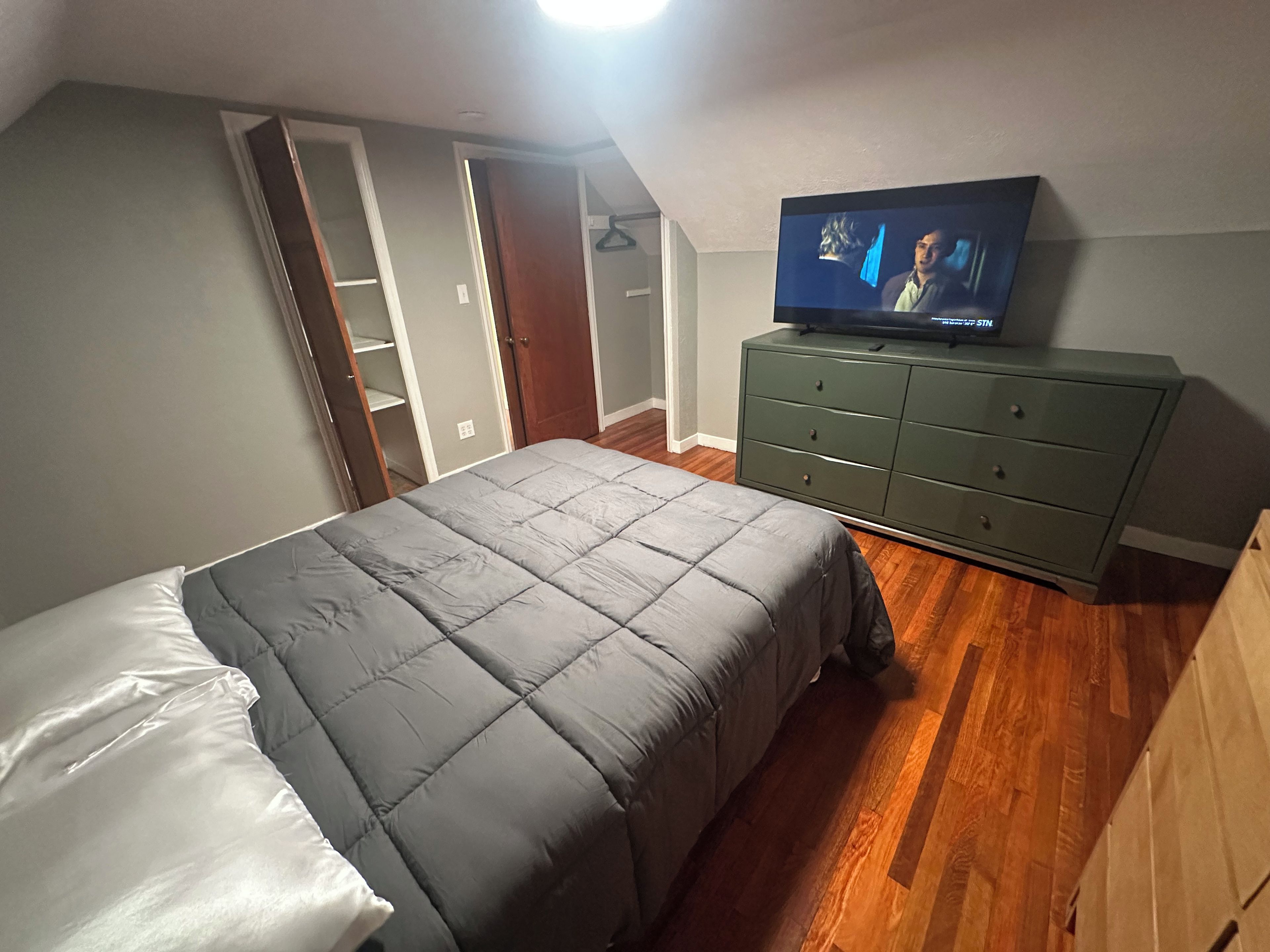Un dormitorio con cama, cómoda, televisor y armario.