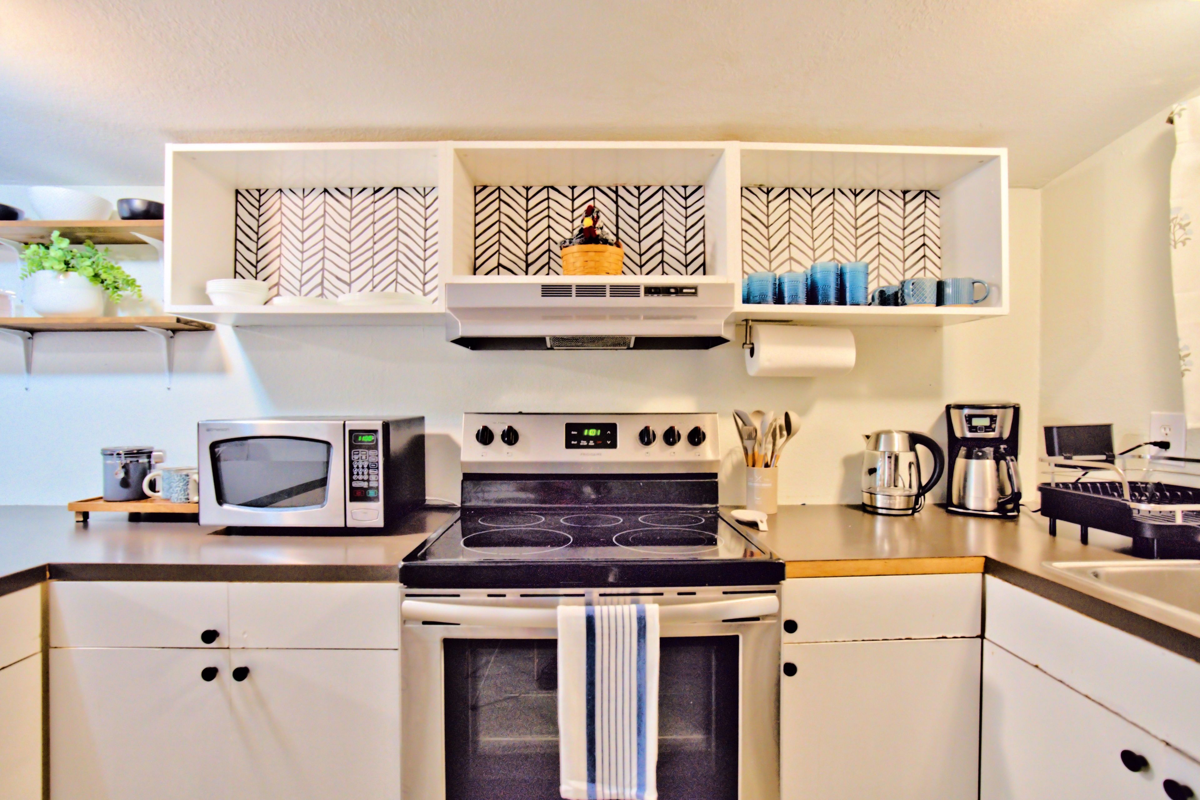 A kitchen with a microwave, stove, oven, and shelves above with patterned tiles.