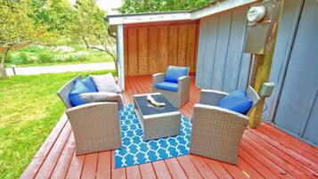 An outdoor patio with wicker furniture, a blue patterned rug, and a wooden deck.
