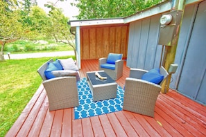 An outdoor patio with wicker furniture, a blue patterned rug, and a wooden deck.