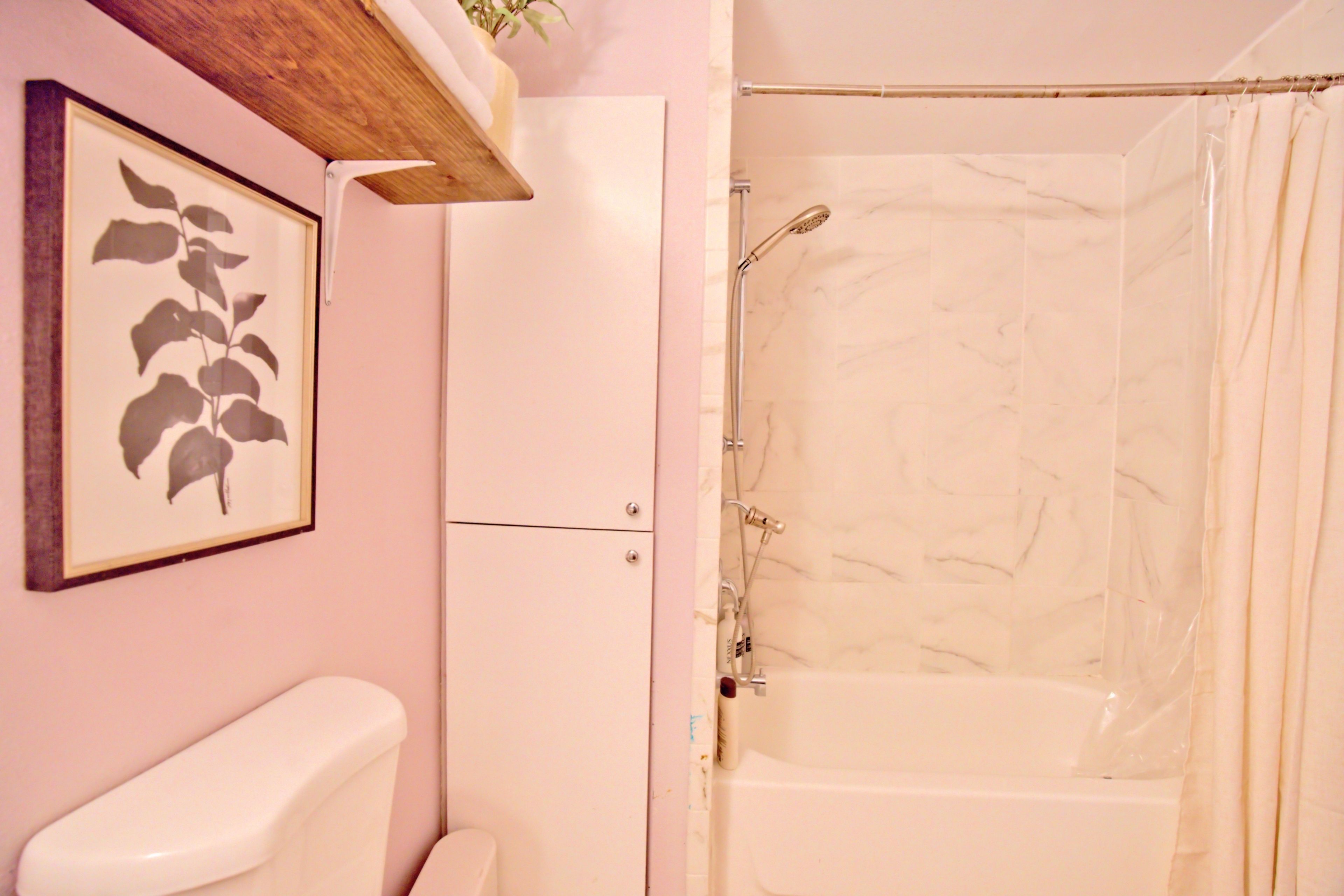 A bathroom with a toilet, a shower with a glass door, and a framed picture on the wall.