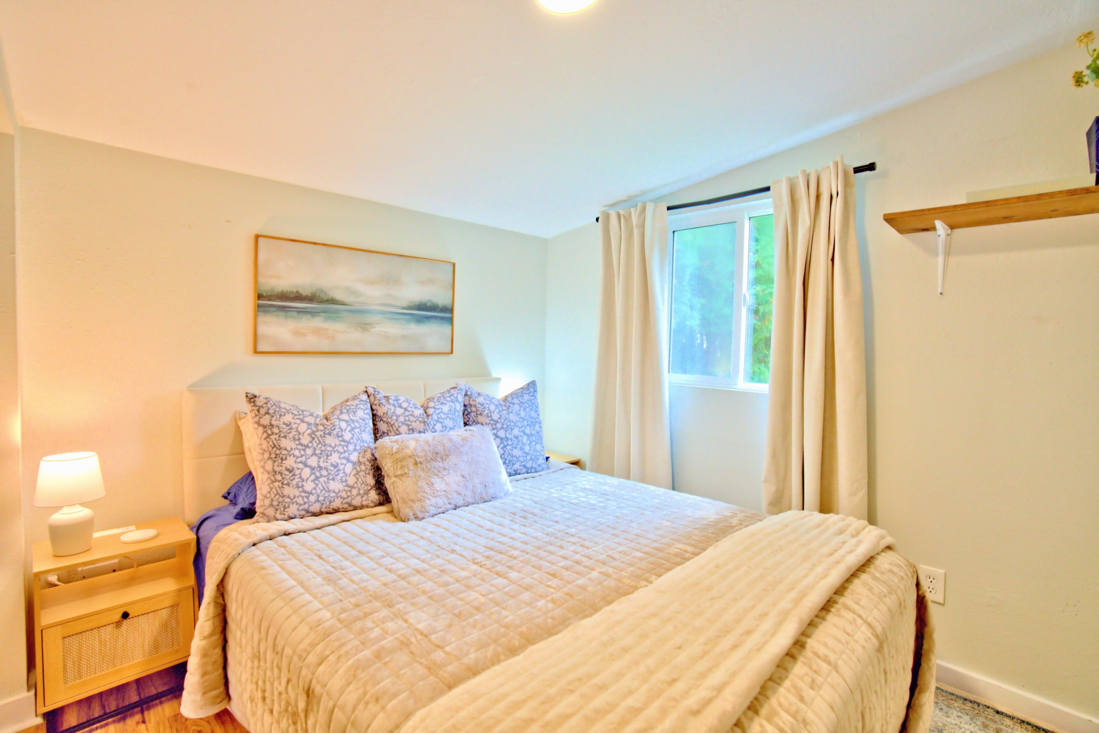 A bedroom with a bed, nightstand, lamp, and a painting on the wall.