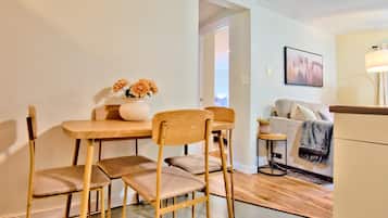 A dining area with a wooden table and chairs, a vase with flowers, and a sofa in the background.