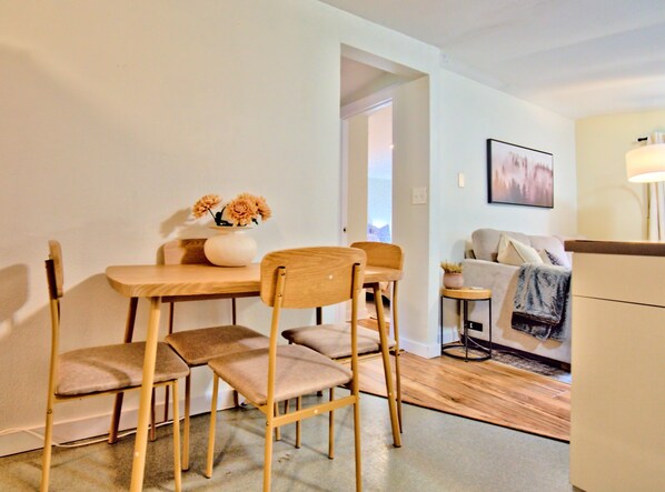 Un coin repas avec une table et des chaises en bois, un vase de fleurs et un canapé en arrière-plan.