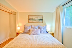 A bedroom with a large bed, a painting on the wall, and a window with curtains.