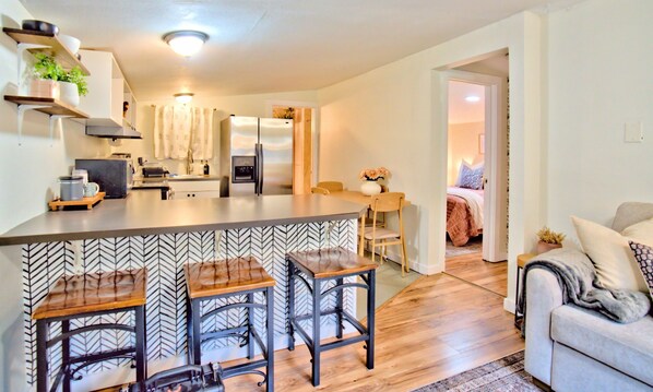 A modern kitchen with a central island, bar stools, and a dining area with a table and chairs.