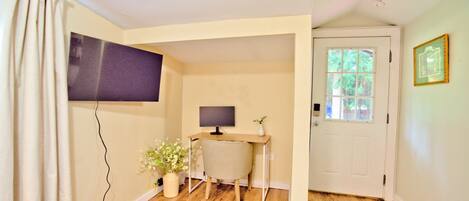 A room with a desk, chair, television, and a door with a window.