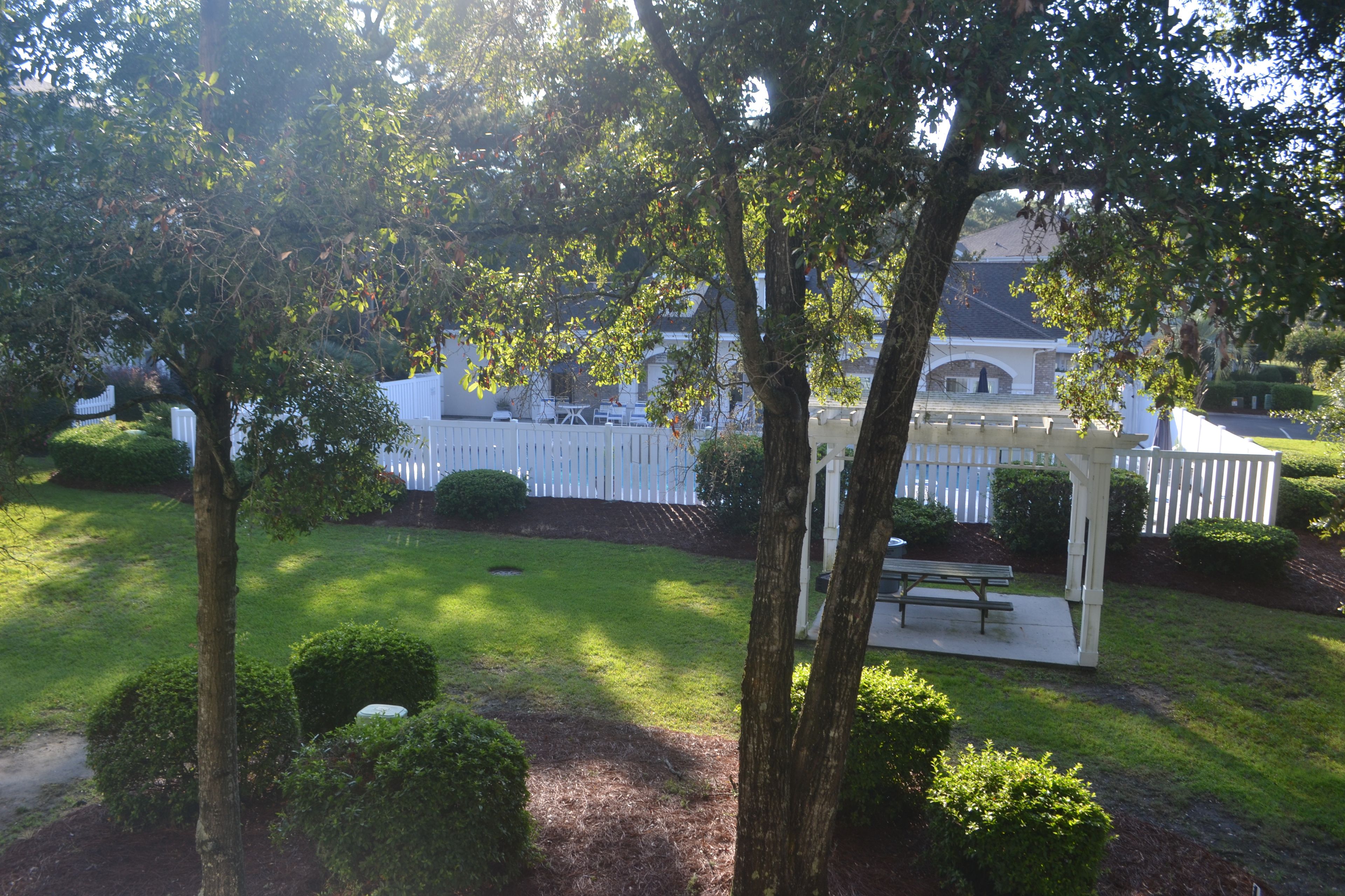 A well-maintained garden with a white fence, a pergola, and a picnic table.
