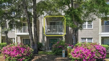 Un edificio de apartamentos de varios pisos con balcones, rodeado de exuberante vegetación y arbustos florecientes.