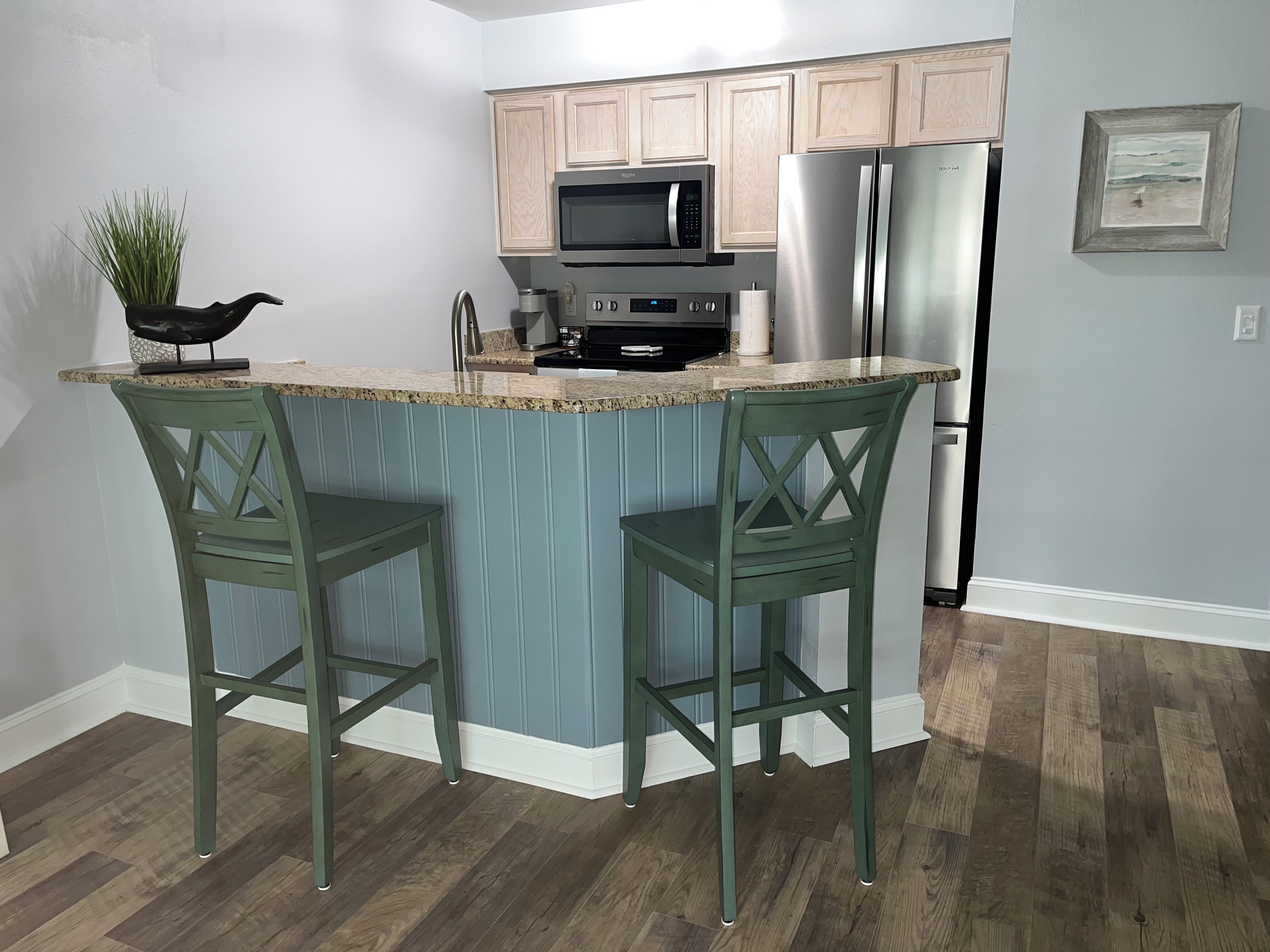 A kitchen with a central island, two bar stools, a microwave, a refrigerator, and wooden cabinets.