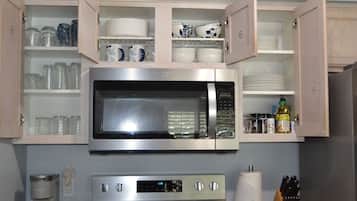 A kitchen with a built-in microwave, a coffee maker, and cabinets with dishes and glassware.