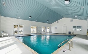 An indoor swimming pool with clear water, surrounded by white walls and a blue ceiling.