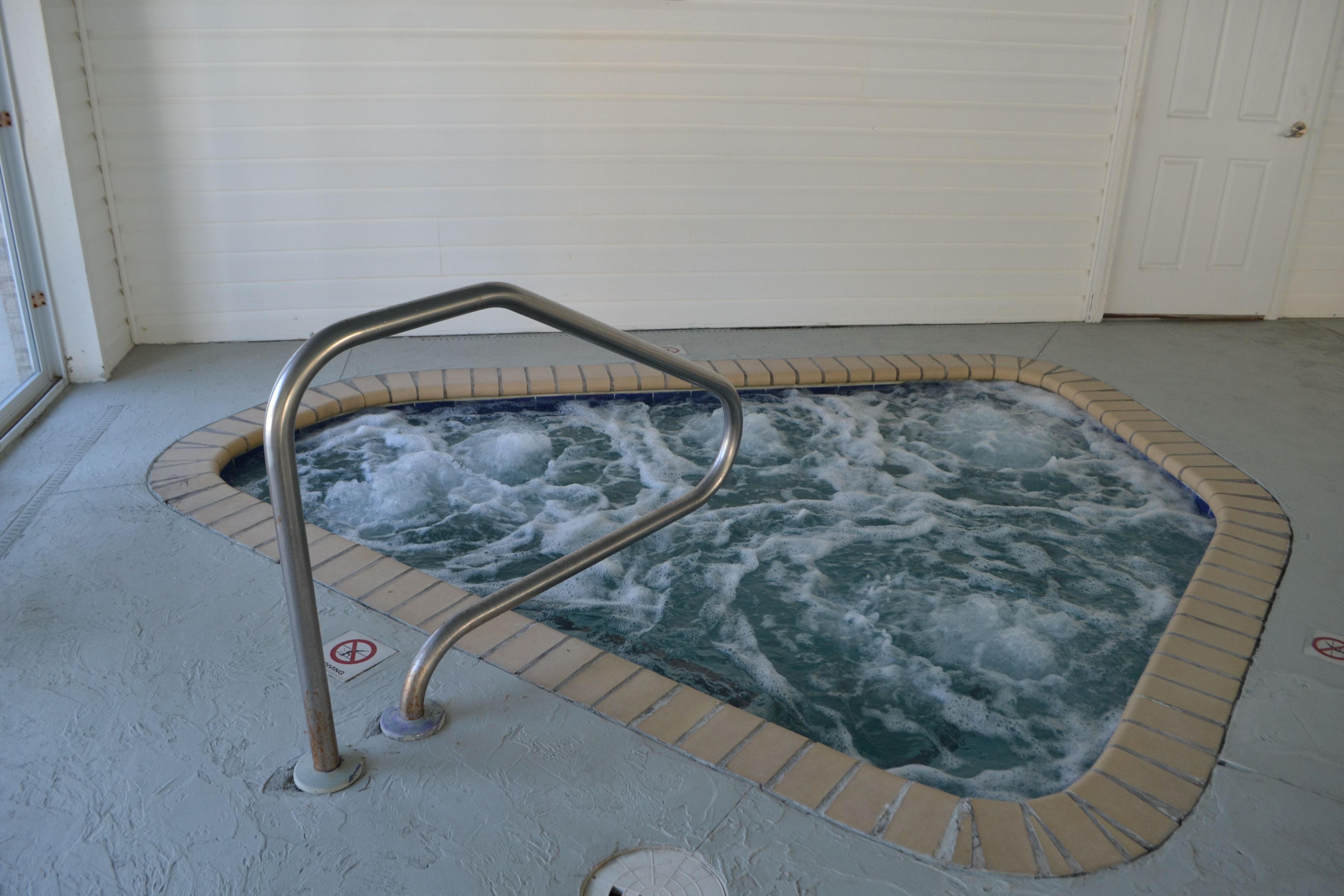 A hot tub with a metal safety rail, surrounded by a tiled border.