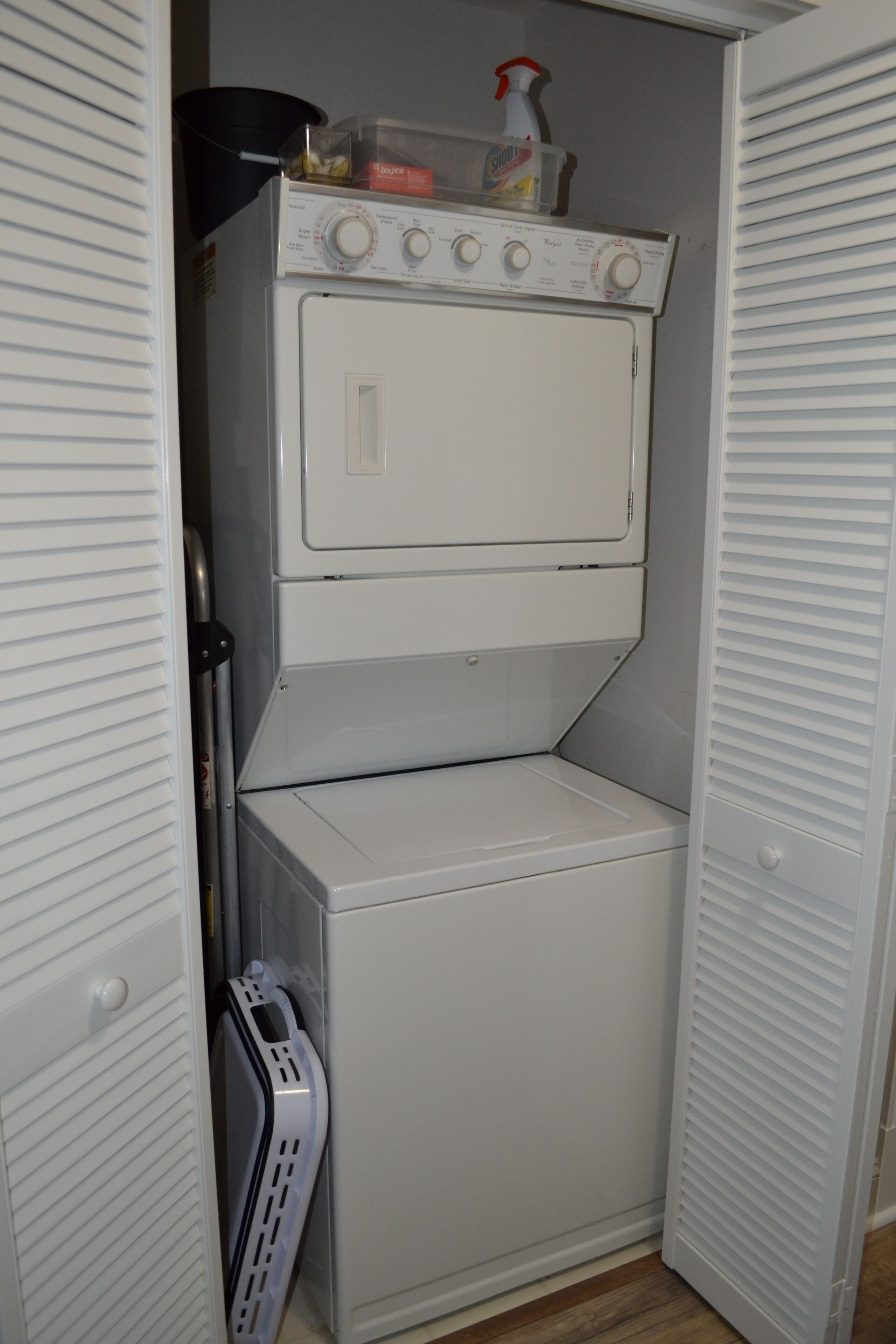 A compact laundry room with a front-loading washer and dryer, a drying rack, and a storage cabinet.