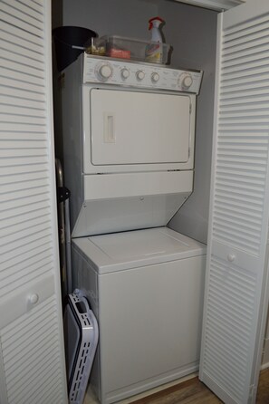 A compact laundry room with a front-loading washer and dryer, a drying rack, and a storage cabinet.