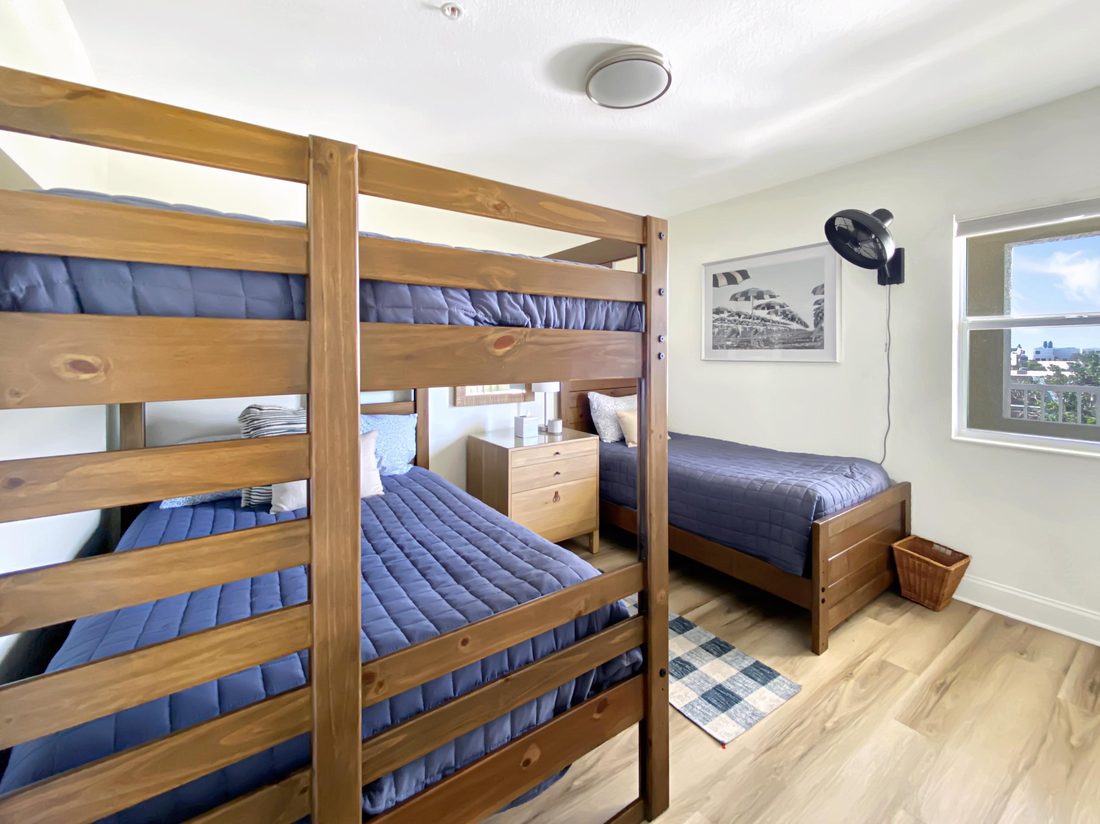 Une chambre avec des lits superposés, un bureau, une chaise, une fenêtre donnant sur un paysage agréable et un luminaire au plafond.