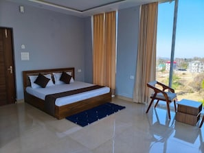 A bedroom with a bed, a desk, and a view of the outside.