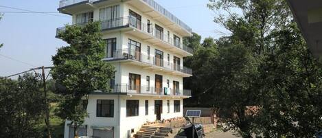 Un edificio residencial de varios pisos con balcones, un coche estacionado en frente y un panel solar en el suelo.