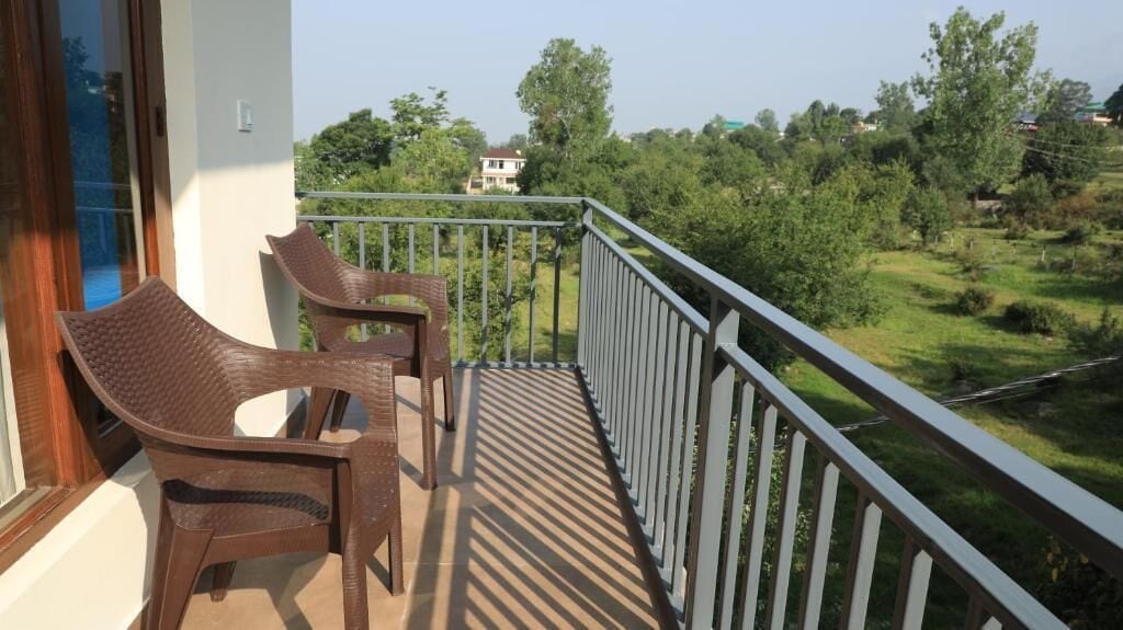 Een balkon met rieten stoelen en een hekwerk, met uitzicht op een groen landschap met bomen en een gebouw in de verte.