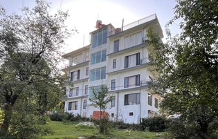 A multi-story residential building with balconies, surrounded by trees and greenery.