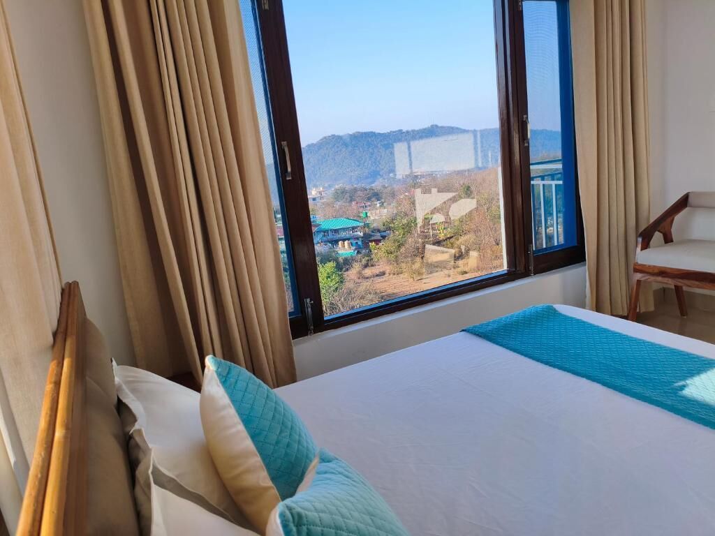 Una camera d'albergo con un letto, vista su un paesaggio lontano e una sedia.