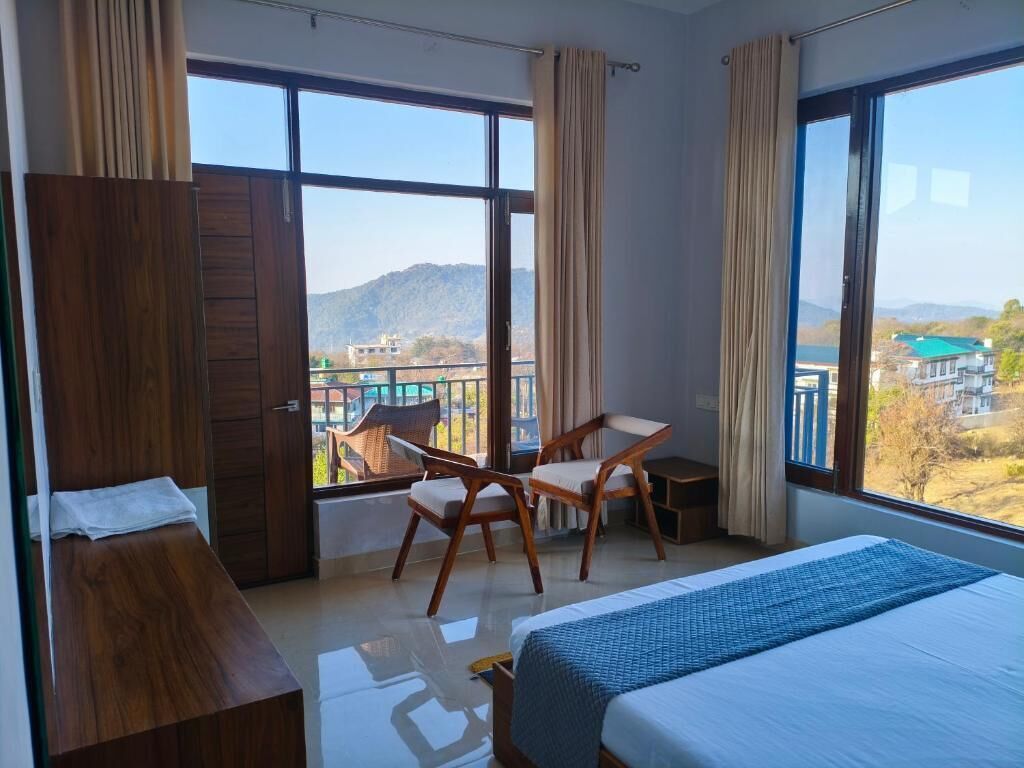 A hotel room with a bed, a desk, and a chair, with large windows offering a view of the outdoors.