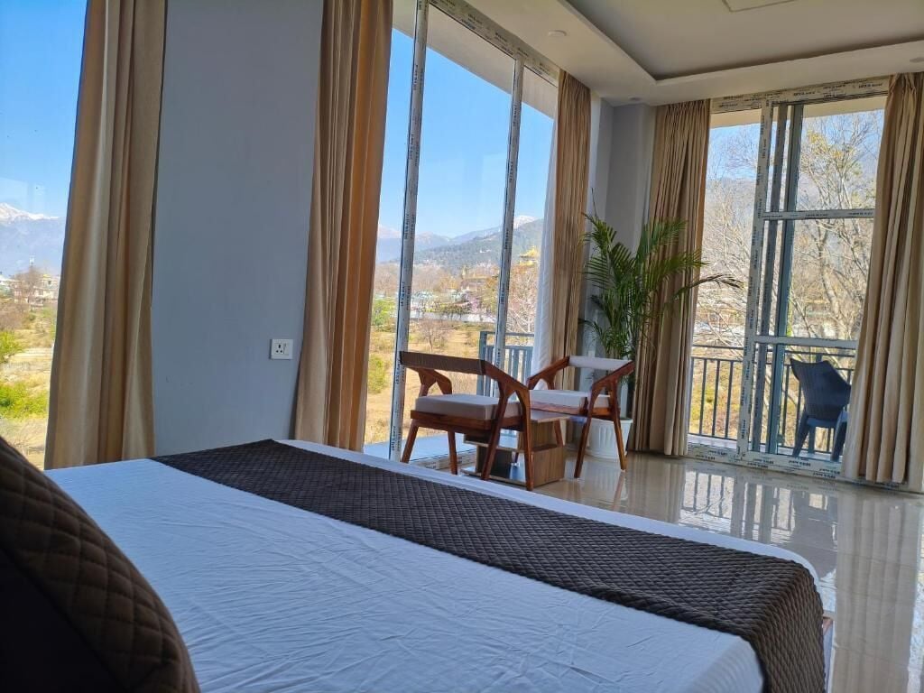 Une chambre d’hôtel avec un grand lit, un balcon offrant une vue sur les montagnes et un coin repas avec des chaises.