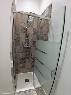 Eine Duschkabine mit Glas, gemusterten Fliesen und einem sichtbaren Abfluss.