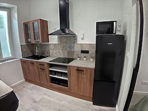Eine moderne Küche mit Holzschränken, einer schwarzen Dunstabzugshaube, einer eingebauten Mikrowelle und einem Edelstahl-Kühlschrank.