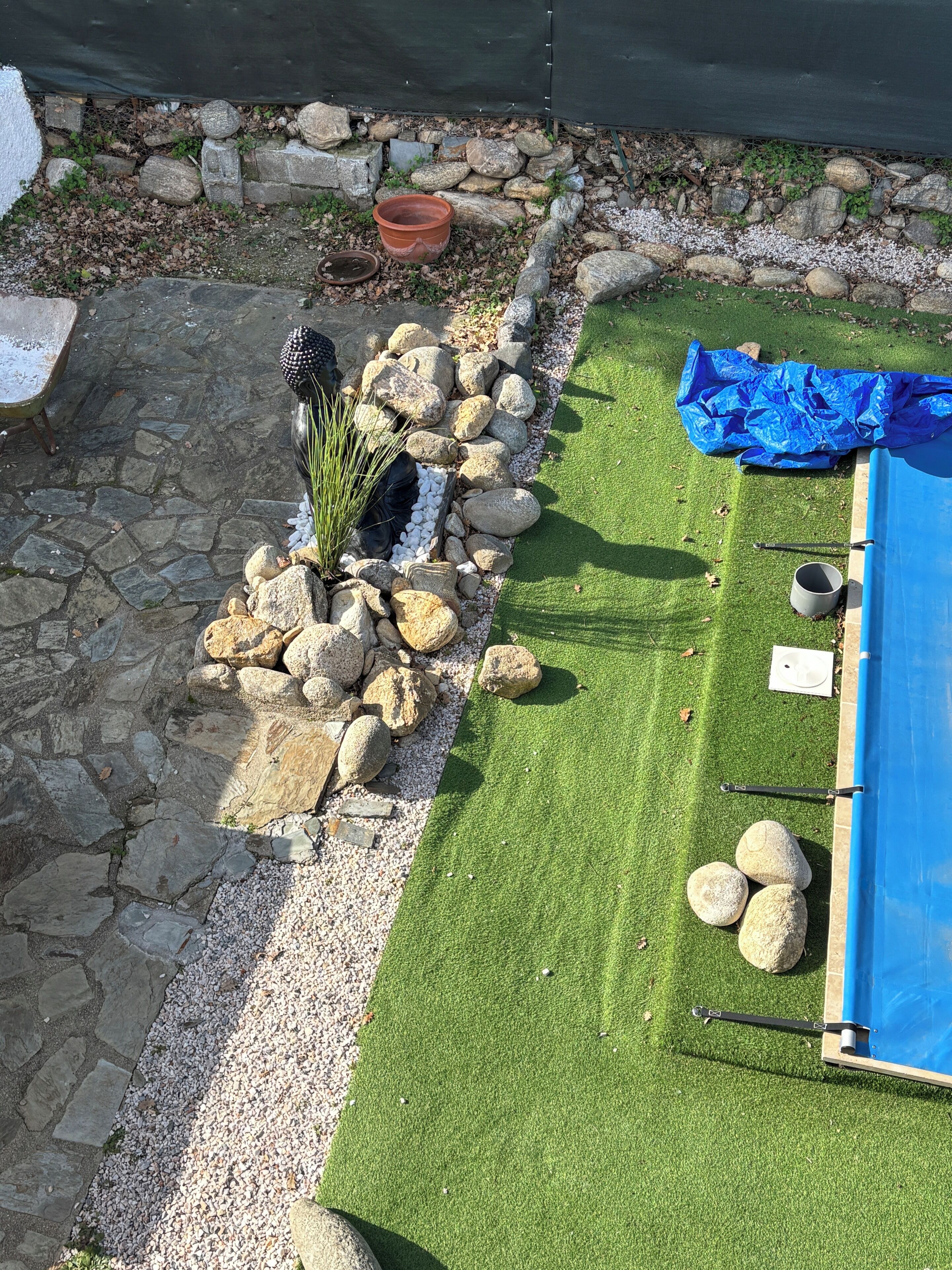 A garden with a stone pathway, a blue tarp, and a pool area.