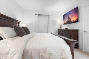 A bedroom with a bed, a nightstand, a dresser, a window with blinds, and a wall-mounted picture. - 2BR Getaway Steps from Disney (Kissimmee)