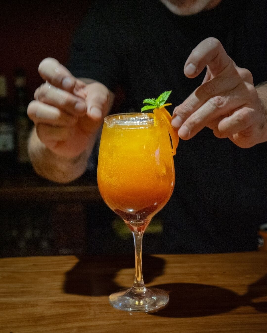 Une personne tenant un verre à cocktail, agrémenté d’une garniture, sur une surface en bois.