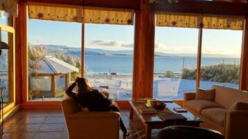Une pièce dotée d’une grande fenêtre donnant sur une plage et des montagnes, et aménagée avec un canapé et une table basse.