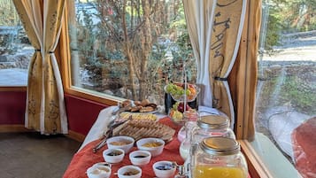 Montaje de un bufé de desayuno con diversos alimentos y bebidas, dispuesto en una mesa con vistas al exterior.