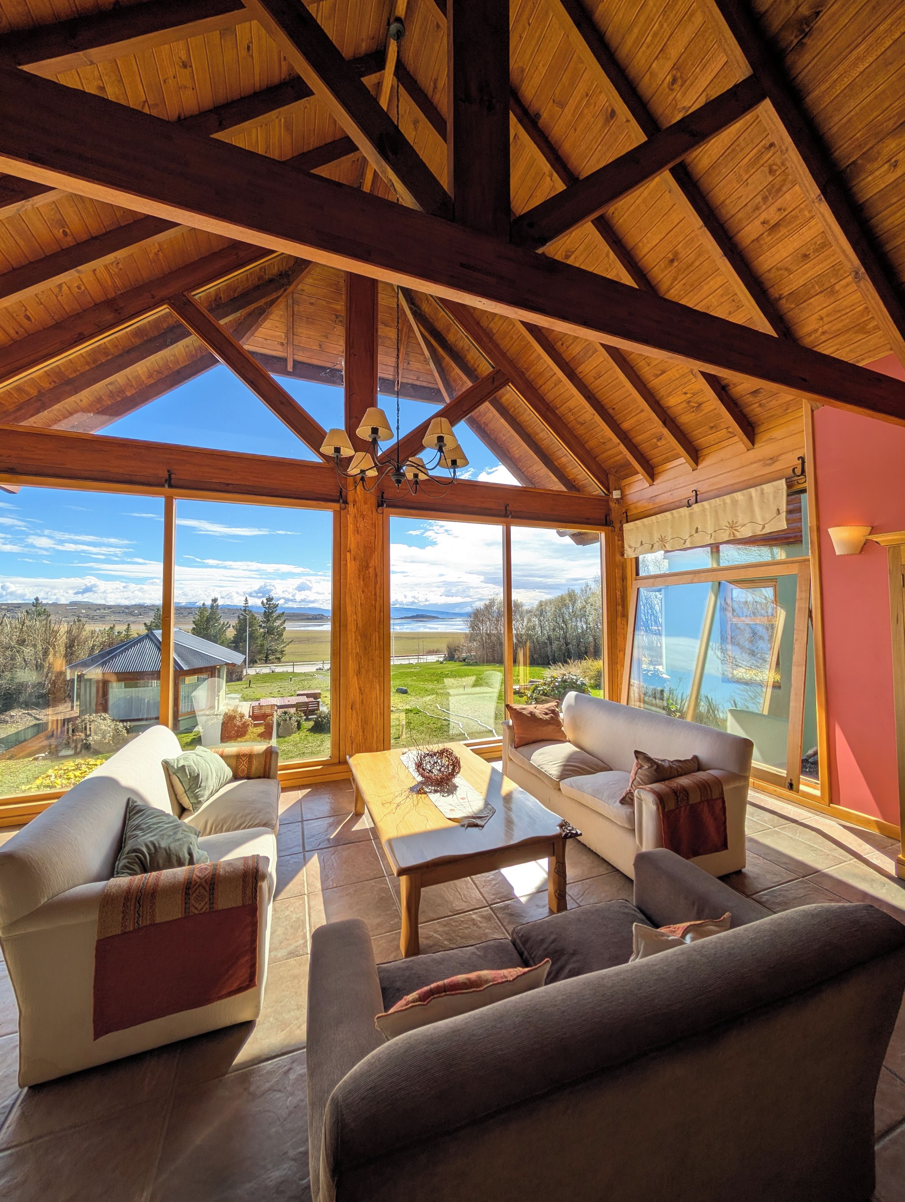 A spacious room with a high ceiling, wooden beams, and large windows offering a view of the countryside.