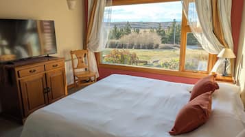 Quarto com cama, cadeira, televisão e janela com cortinas.