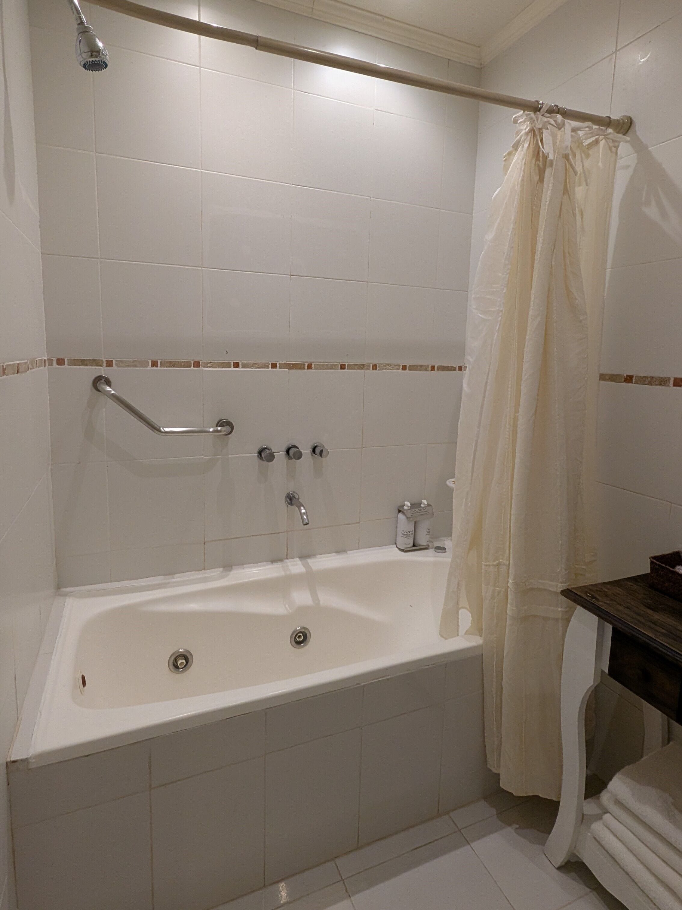 A bathroom with a bathtub, a showerhead, a grab bar, and a towel rack.