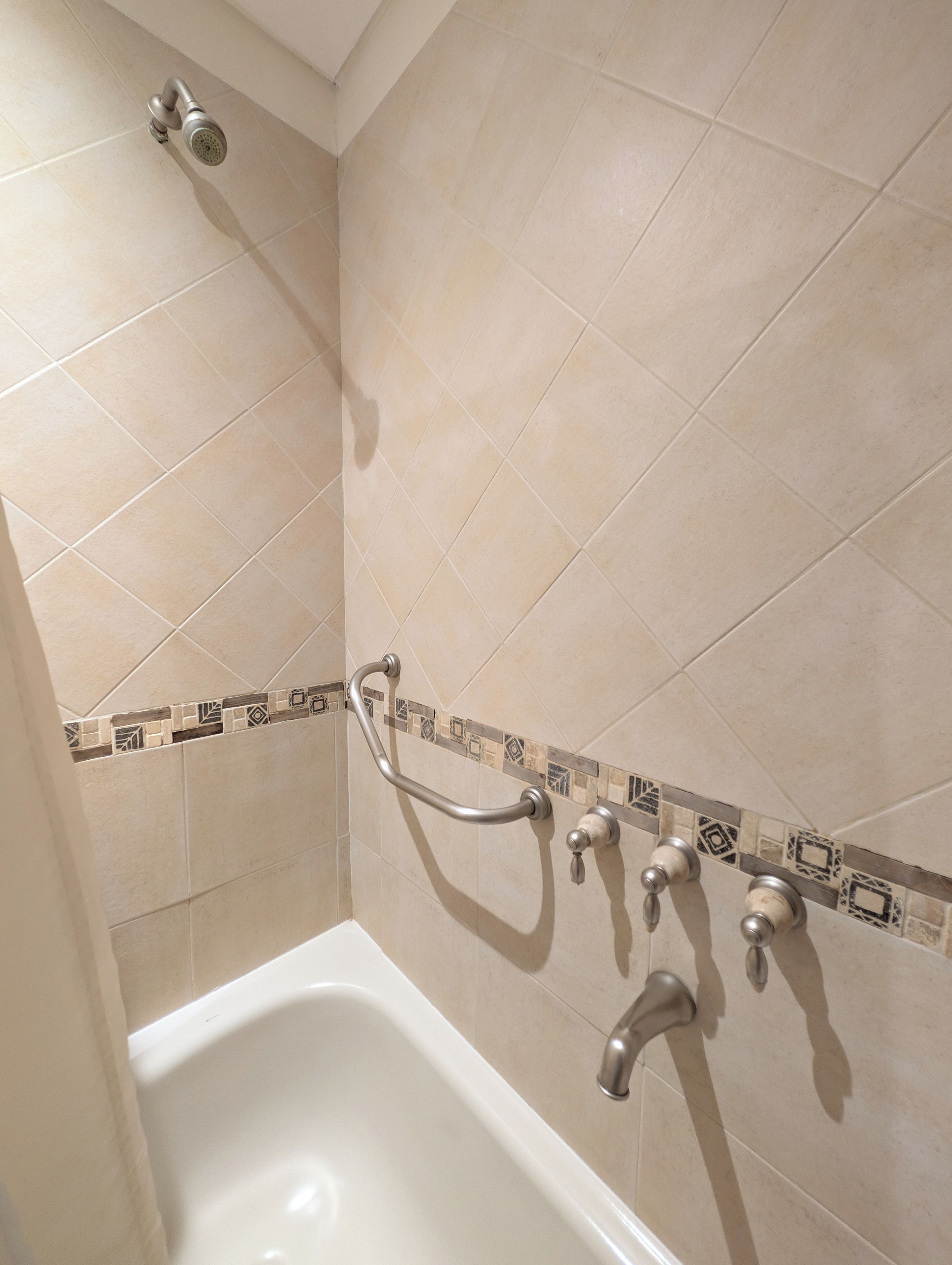 A bathroom with a bathtub, a shower head, and a grab bar.