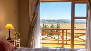 Un dormitorio con cama, mesita de noche, lámpara y vistas a un balcón con barandilla.