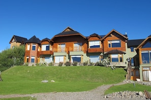 A multi-story wooden house with a sloped roof, a stone pathway, and a grassy lawn. - Hostería Los Hielos (El Calafate)