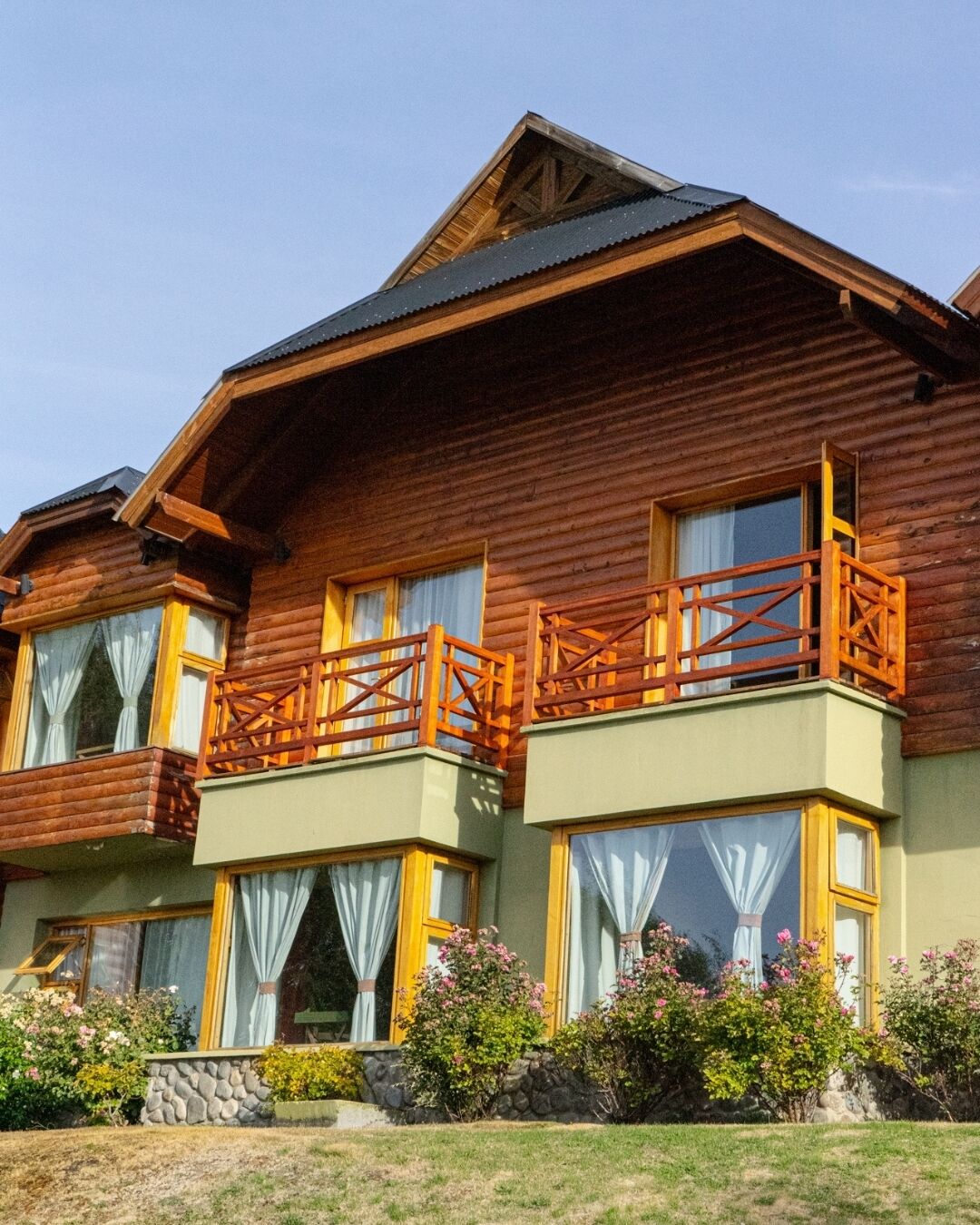 Une maison en bois à deux étages, dotée d’un balcon, de grandes fenêtres et de fondations en pierre.