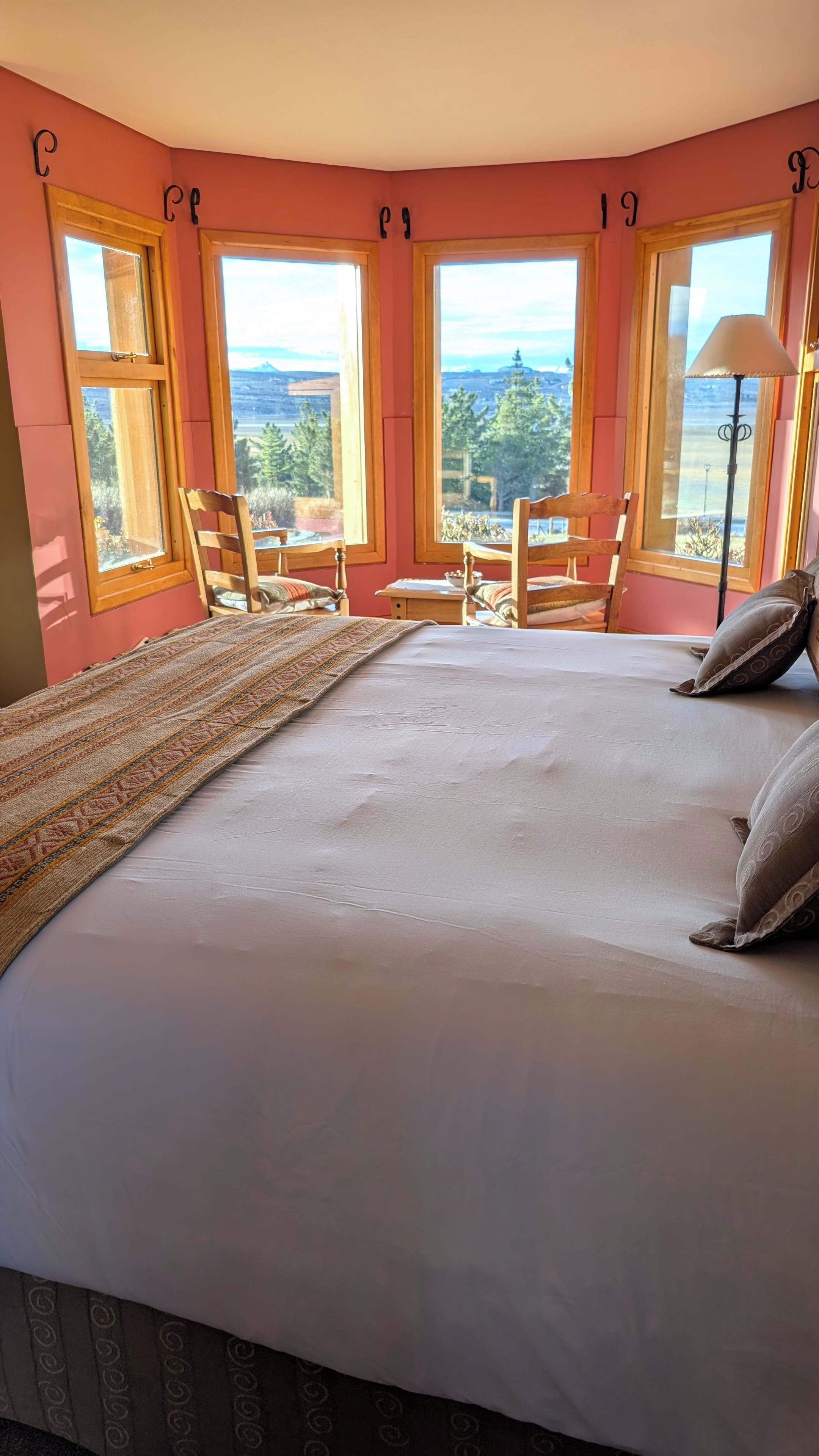 Quarto com cama grande, duas cadeiras, uma mesinha e vista para o exterior.