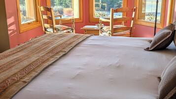 Quarto com cama grande, duas cadeiras, uma mesinha e vista para o exterior.