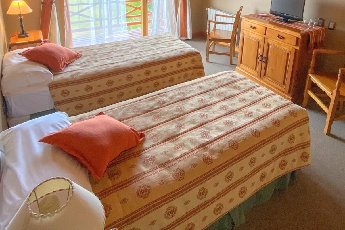 A room with two beds, a desk with a computer, and a window with curtains.
