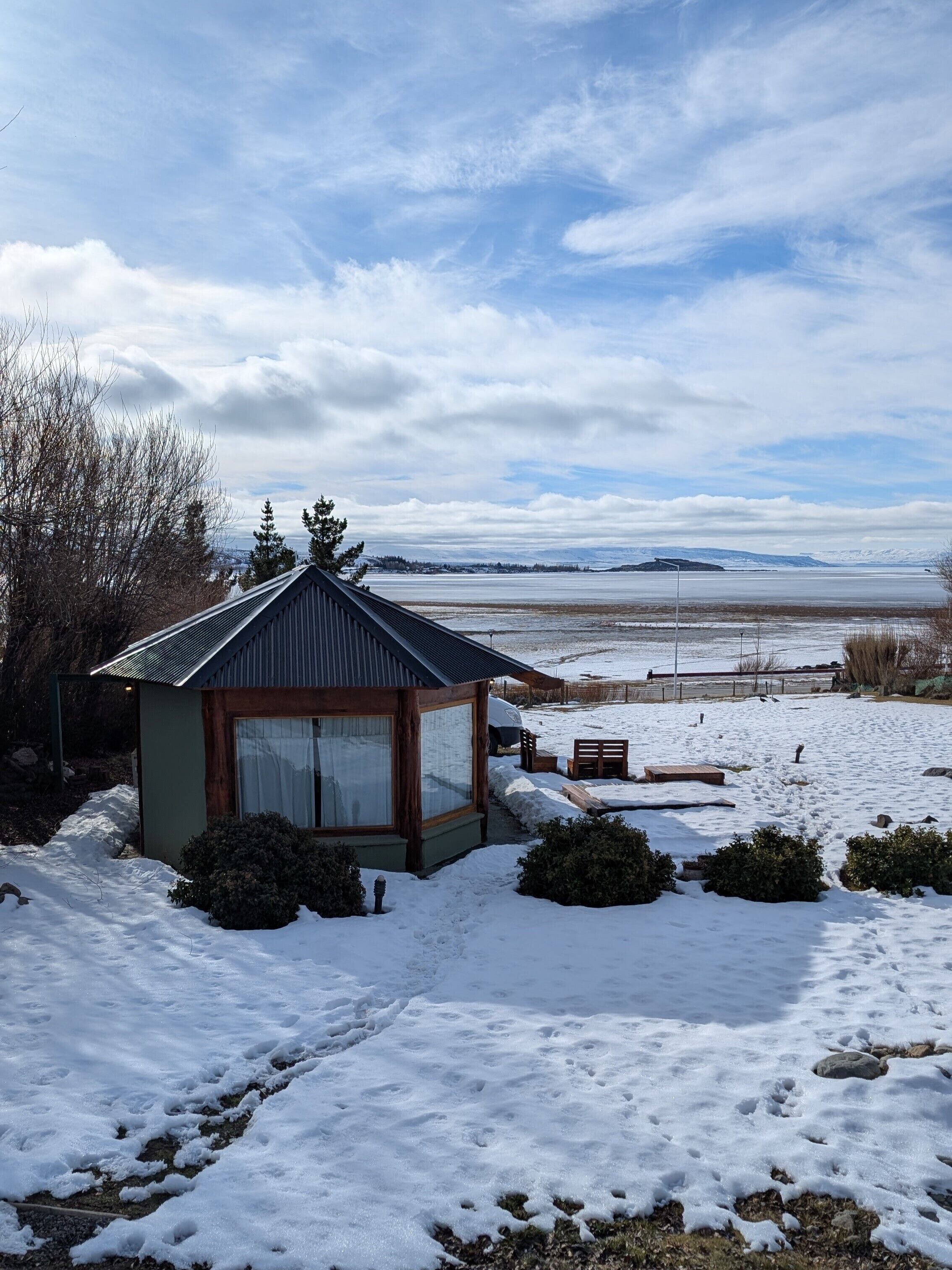 A small cabin with a sloped roof, a glass door, and a view of a snowy landscape.