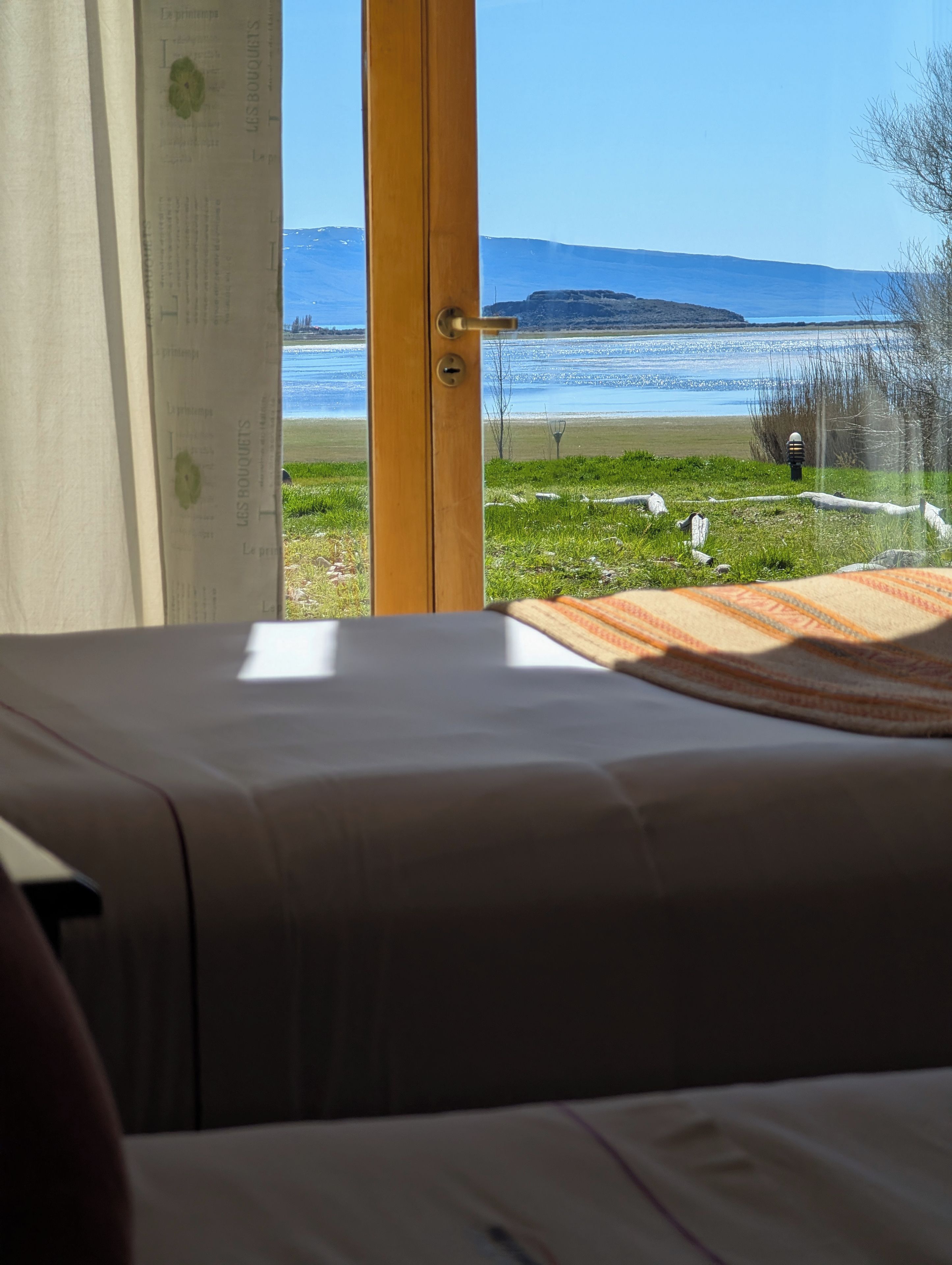 Una stanza con un letto, una finestra e vista su un lago e montagne in lontananza.