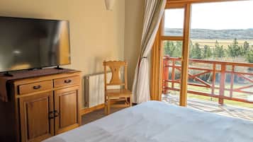 Une chambre à coucher avec un lit, un téléviseur posé sur une commode en bois, une chaise et une vue sur un balcon doté d’une balustrade.