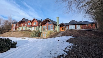 Une rangée de chalets en rondins, avec une allée enneigée et un escalier en bois menant à l’entrée.