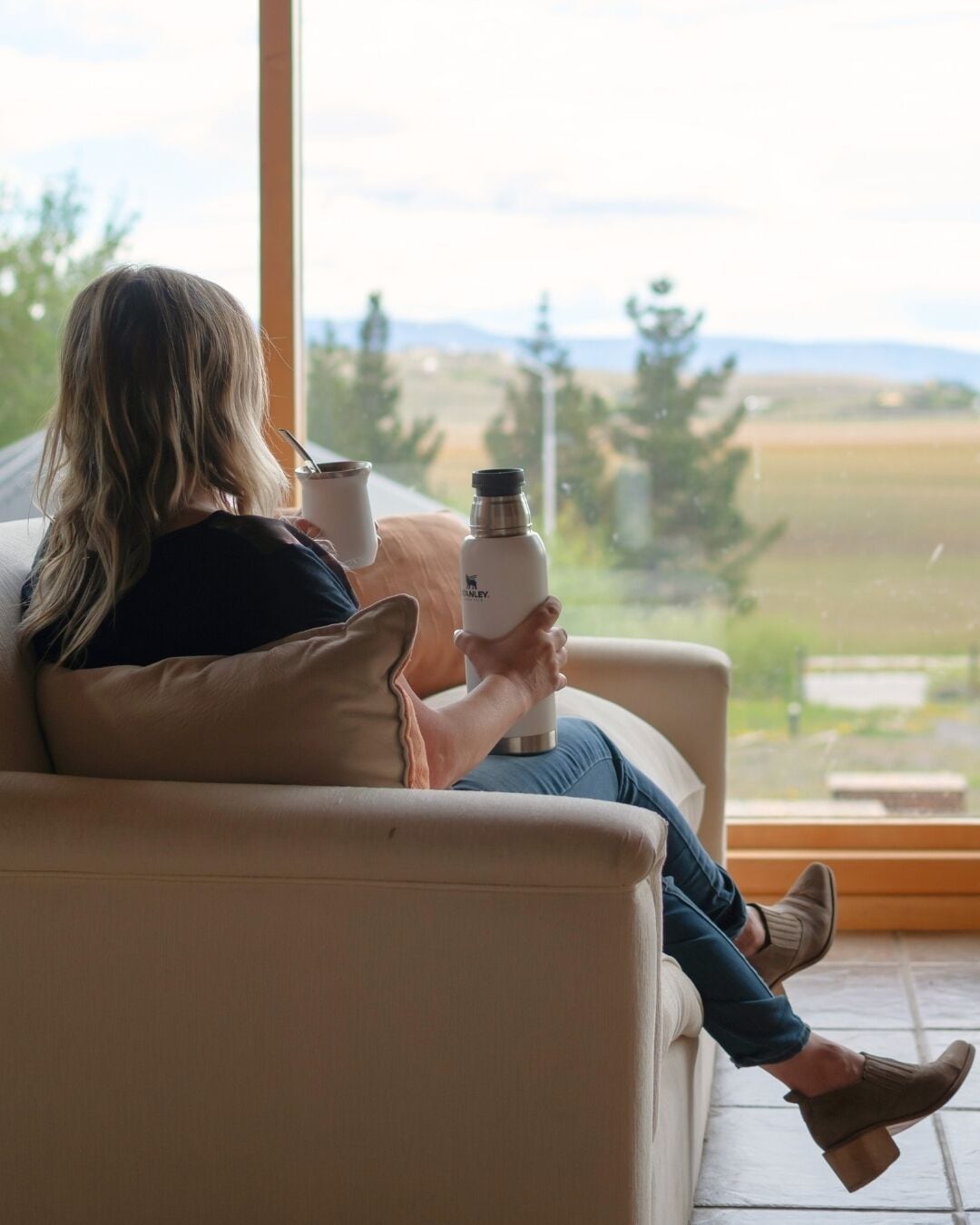 Une personne assise sur un canapé, devant une fenêtre donnant sur un paysage.