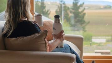Une personne assise sur un canapé, devant une fenêtre donnant sur un paysage.